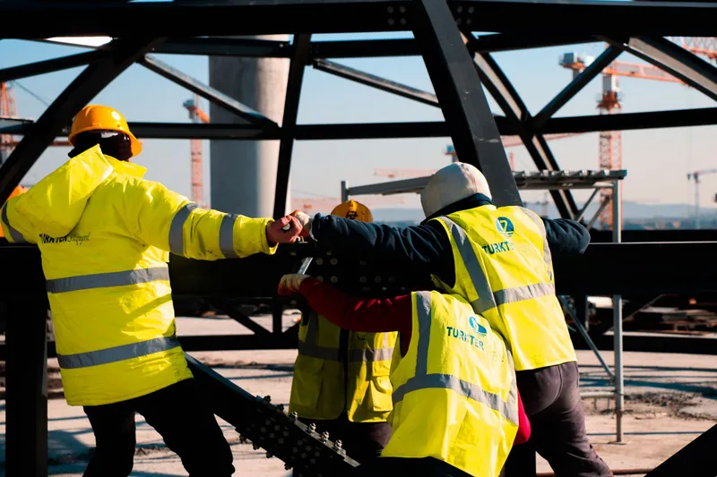 Workers in high-visibility jackets shaking hands on a steel structure