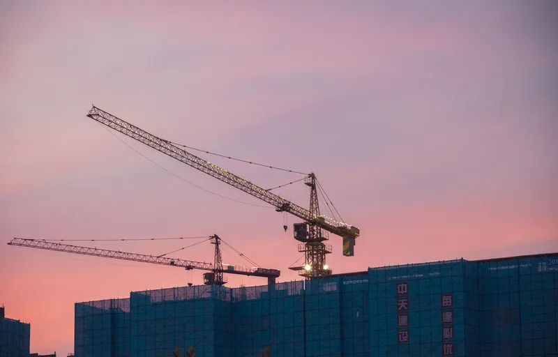 Tower cranes over a building under construction at sunset